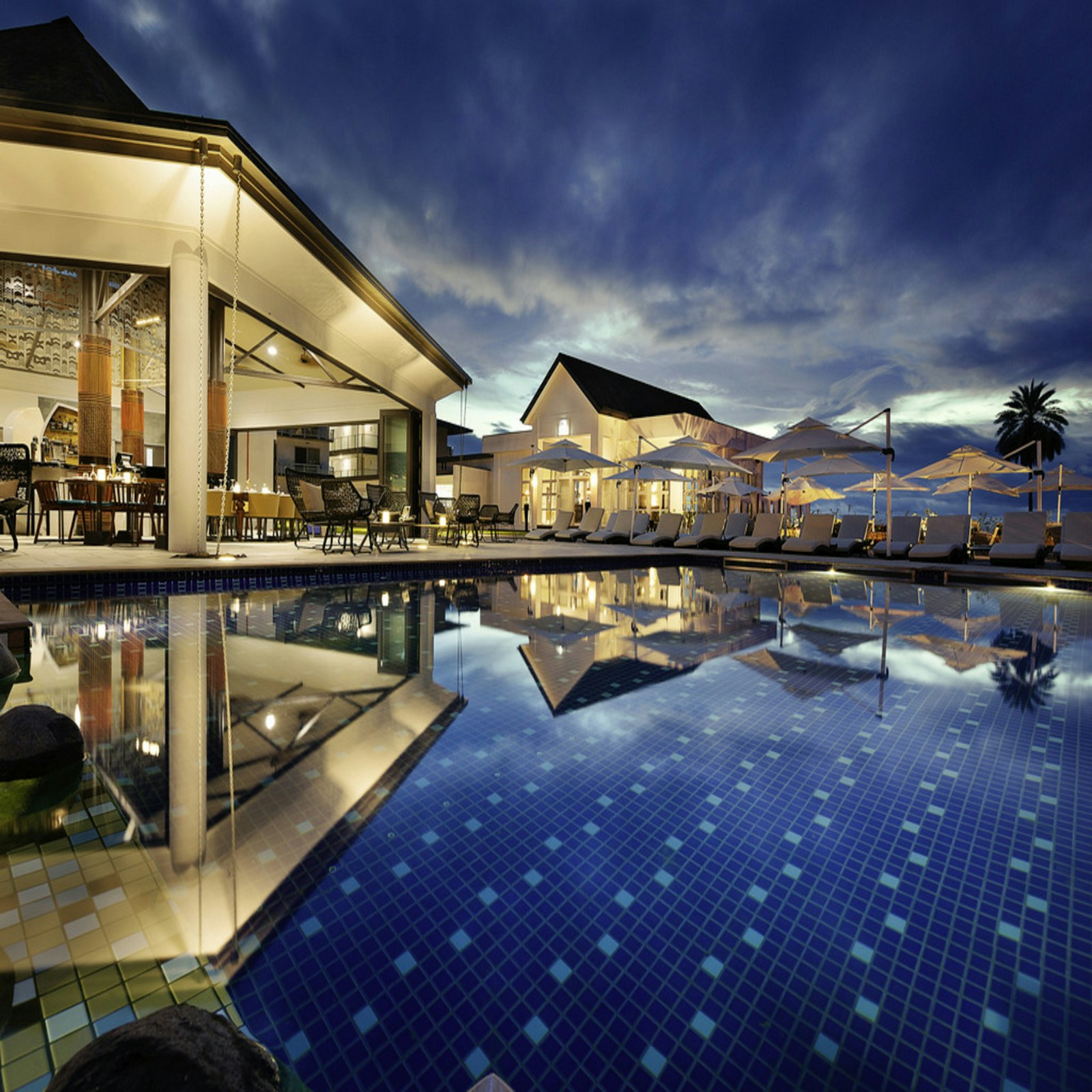 A softly lit hotel beside a blue swimming pool at dusk
